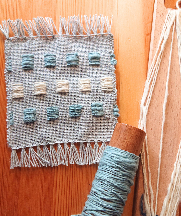 手織りワークショップで制作するミニコースターのサンプル。浮き織りでデザインされた四角模様と優しいブルーグレーの糸が特徴的。